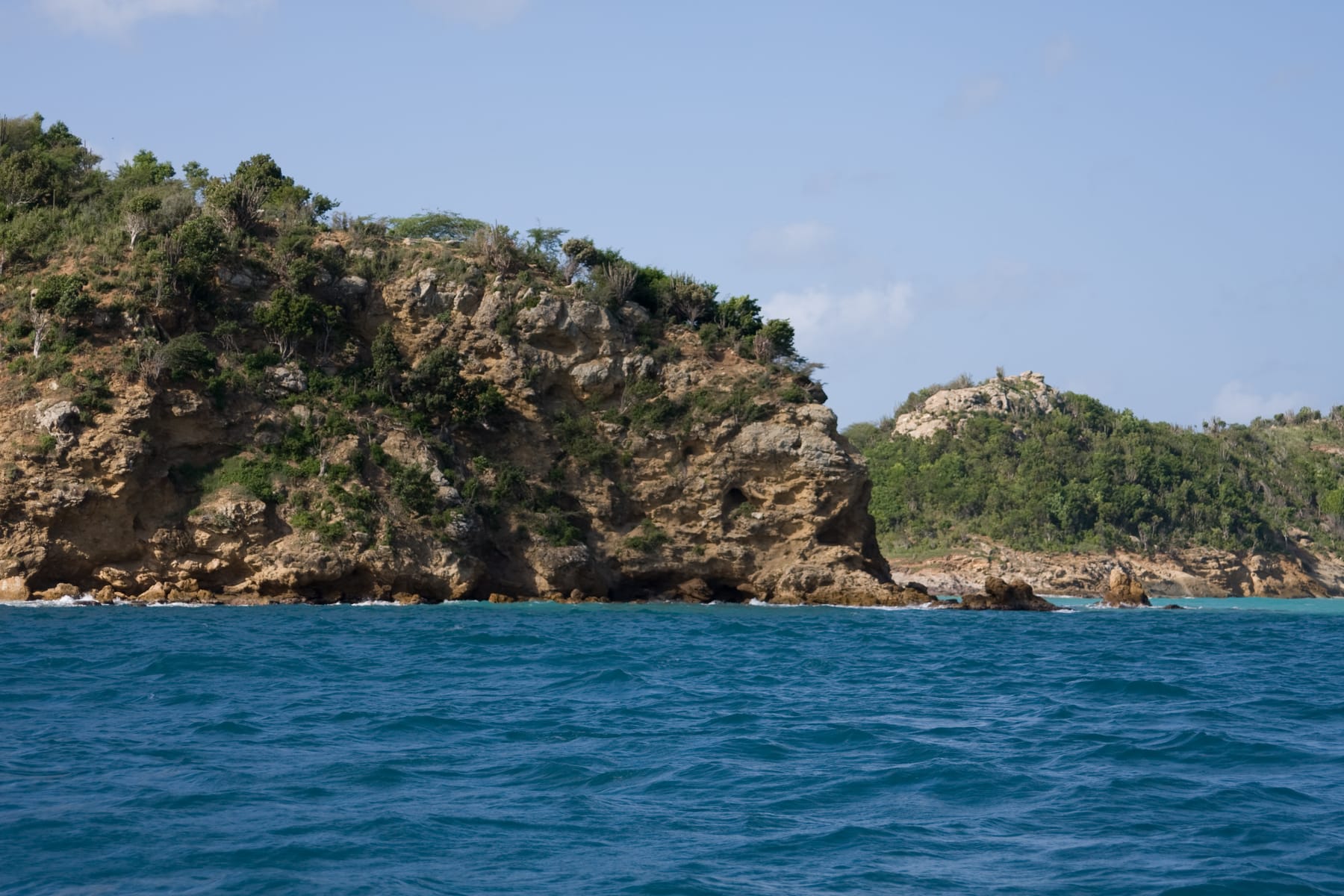 Rocky Antigua shoreline with turquoise sea and low green hills